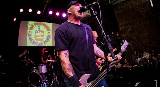 Sem frescuras: CJ Ramone canta na frente do palco com o logo 'American punk' projetado no fundo