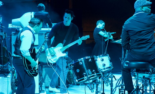 Imagem mostra a banda pela lateral do palco, com o baixista Dominic Davies e o batera Dau Jones