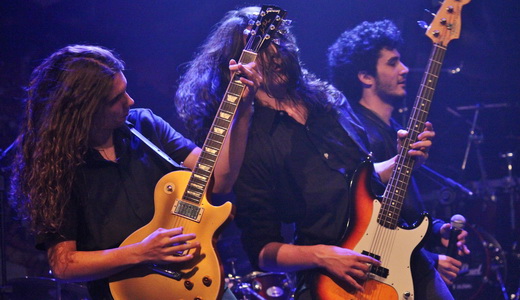 Odysseya: o guitarrista Vinicius Mira, o baixista Vitor Vieira e o vocalista Felipe da Silva agitando no palco